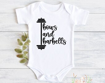 May include: White baby onesie with the text "Bows and Barbells" in black script, accompanied by a barbell graphic. The onesie is made of soft material and is designed for infants. The onesie is a cute and stylish baby garment.