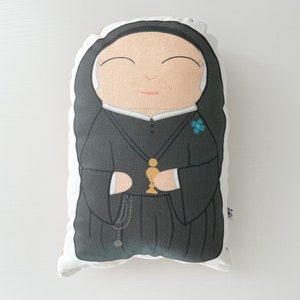 May include: A black and white pillow with a cartoon image of a nun holding a chalice. The nun is wearing a black habit and a white wimple. The chalice is gold and has a small cross on it.