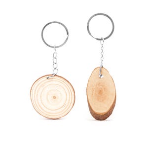 Könnte beinhalten: Zwei Holz-Schlüsselanhänger mit silberfarbenen Metallringen und Ketten. Einer ist eine runde Holzscheibe, der andere ein ovales Stück. Das Holz hat eine natürliche, hellbraune Farbe.