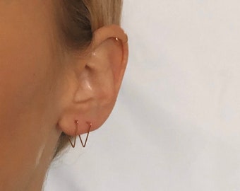 May include: A close-up of a person's ear with two small gold hoop earrings. The earrings are in the shape of a V.
