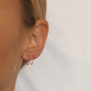 May include: A close-up of a person's ear with two small gold hoop earrings. The earrings are in the shape of a V.