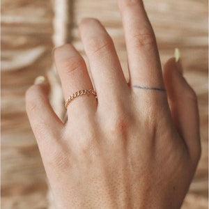 May include: A gold chain ring on a finger.