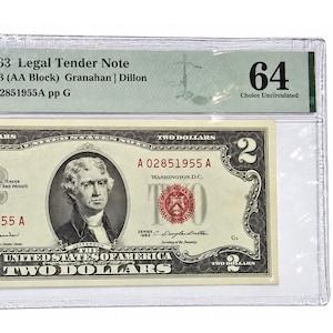 May include: A 1963 United States two-dollar legal tender note featuring a portrait of Thomas Jefferson, enclosed in a PMG graded plastic holder. The bill displays red serial numbers, a red seal, and the text Two Dollars across the front.