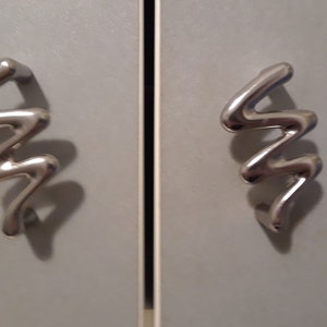 May include: Two silver cabinet door handles with a wavy, abstract design.