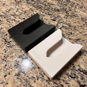 Puede incluir: Dos porta tarjetas minimalistas, uno negro y otro blanco, con la palabra "HUCHO" impresa en ellos.