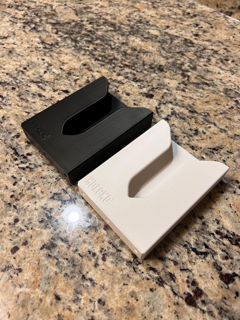 Puede incluir: Dos porta tarjetas minimalistas, uno negro y otro blanco, con la palabra "HUCHO" impresa en ellos.