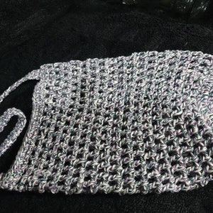 May include: A crocheted bag with a long strap, made with white, purple, and black yarn.