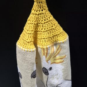 May include: A handmade yellow crochet kitchen towel holder with a button closure. The towel features a print of a white cockatoo with yellow crest feathers. The bottom of the towel has the text "Don't"