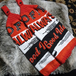 May include: Two red and white kitchen towels with the words "Always Good Idea" printed on them. The towels have a black stripe and a crocheted red top with a button closure. The towels are lying on a faux fur surface.