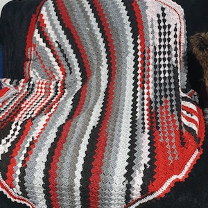 Puede incluir: Una manta de ganchillo con un patrón ondulado en rojo, negro, blanco y gris.