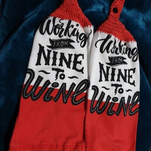 May include: Two white and red kitchen towels with the text "Working From Nine To Wine" in black script. The top portion is red crochet with a black button. The bottom half of the towels are red.