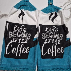 May include: Two hanging kitchen towels with a teal crochet top and bottom trim. The towels are white with a black coffee cup design and the words "life BEGINS AFTER Coffee" in white lettering.