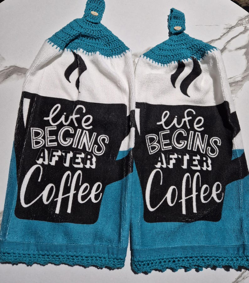 May include: Two hanging kitchen towels with a teal crochet top and bottom trim. The towels are white with a black coffee cup design and the words "life BEGINS AFTER Coffee" in white lettering.