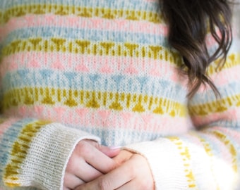 May include: A pastel-colored sweater with horizontal stripes in pink, light blue, and yellow. The sweater has a high neckline and long sleeves with white cuffs. The knitted design features a repeating pattern of small shapes.