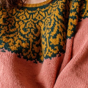 Puede incluir: Un suéter de punto rosa y amarillo mostaza con un patrón geométrico alrededor del cuello.