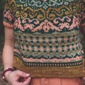 May include: A cropped knitted jumper with a colourful geometric pattern in shades of green, pink, and gold. The jumper has short sleeves and a round neckline.