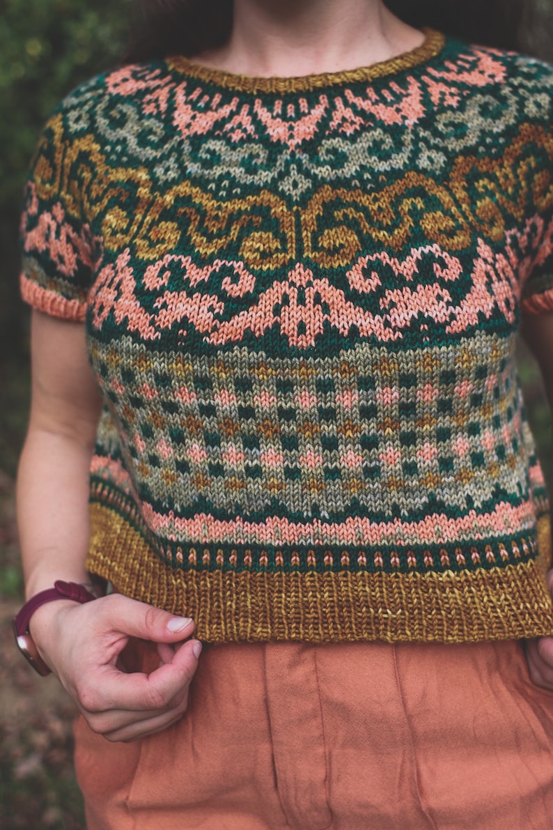 May include: A cropped knitted jumper with a colourful geometric pattern in shades of green, pink, and gold. The jumper has short sleeves and a round neckline.