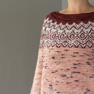 May include: A knitted jumper with a pink and white geometric pattern on the top half and a speckled pink pattern on the bottom half.