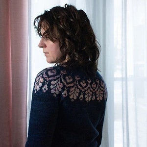 Può includere: Una donna indossa un maglione blu scuro con un motivo floreale rosa e bianco sul collo.
