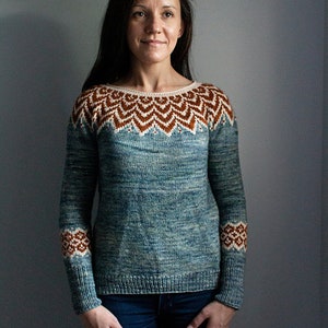 May include: A blue knitted sweater with a brown and white geometric pattern on the yoke and cuffs.