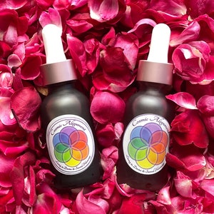 May include: Two dark brown glass bottles with dropper tops and white labels. The labels have a colorful mandala design and the text "Cosmic Alignment Living in Divine & Sacred Harmony". The bottles are surrounded by pink rose petals.