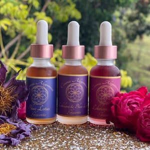 May include: Three glass bottles with dropper tops and labels that say "Cosmic Alignment". The bottles are filled with different colored liquids. The labels also say "Blue Lotus Glycerite", "Lokelani & Blue Lotus Glycerite", and "Lokelani Glycerite".
