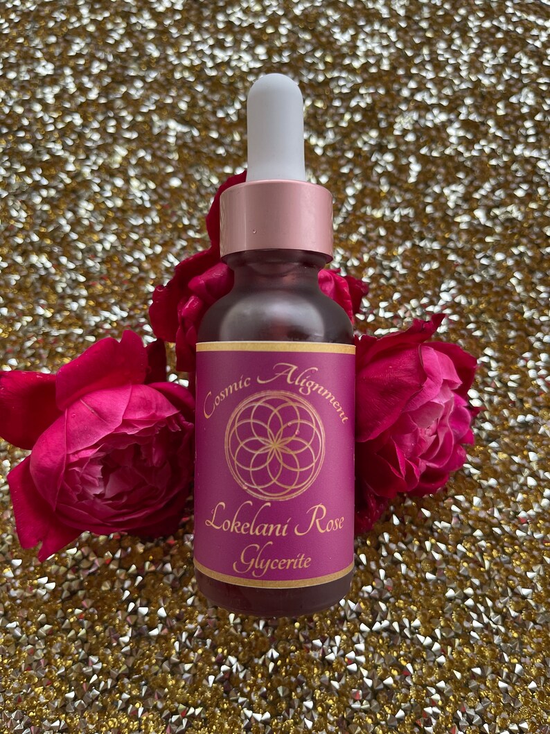 May include: A small glass bottle with a dropper top, filled with a pink liquid. The bottle has a label that reads "Cosmic Alignment Lokelani Rose Glycerite" with a pink and gold geometric design.