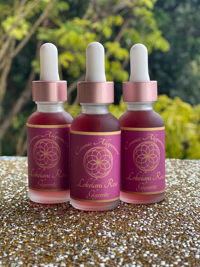 May include: Three glass bottles with dropper tops filled with a pink liquid. Each bottle has a label with the text "Cosmic Alignment" and "Lokelani Rose Glycerite".