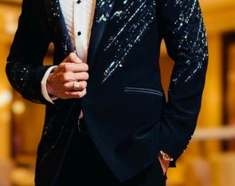 Puede incluir: Chaqueta de esmoquin negra con adornos de lentejuelas en las mangas y los hombros. La chaqueta se combina con pantalones negros, una camisa blanca y una pajarita negra. La imagen también incluye el texto "AFFASHION MEN'S WOMEN COLLECTION."