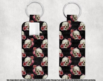 May include: A black key chain with a white skull and pink rose pattern. The key chain has a silver ring and a clear plastic insert for a hand sanitizer bottle.