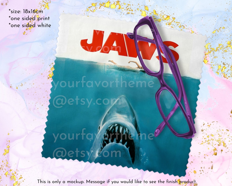 Puede incluir: Un pa&ntilde;o de limpieza de microfibra con un dise&ntilde;o de p&oacute;ster de la pel&iacute;cula Jaws. El p&oacute;ster presenta la boca de un tibur&oacute;n con dientes afilados y el texto "JAWS". El pa&ntilde;o mide 18 pulgadas por 16 pulgadas.