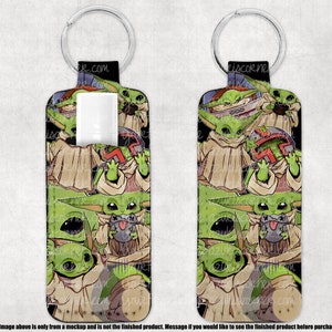 May include: A lip balm holder with a keychain, featuring a repeating pattern of a green alien character with large eyes and a tan robe. The background is black. The holder has a black top with a silver ring.