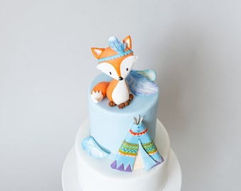 May include: A two-tiered cake decorated with a fondant fox wearing a blue and white headdress, a blue teepee, and blue feathers. The cake is frosted in light blue and white.