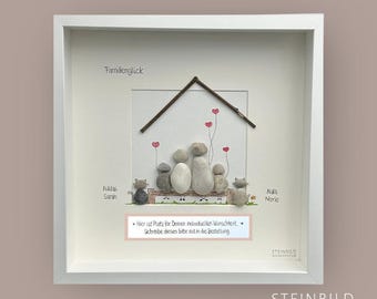 May include: A white framed picture with a stone art piece depicting a family of five with two cats. The family is sitting on a bench under a house with a brown roof. The words "Familienglück" and "STEINBILD MANUFAKTUR" are printed on the picture. The text "Hier ist Platz für Deinen individuellen Wunschtext. Schreibe diesen bitte mit in die Bestellung." is printed on a pink banner.