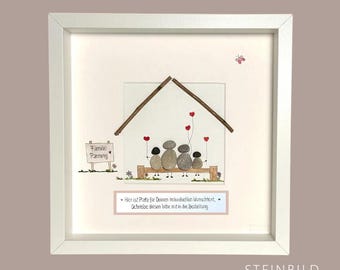 May include: Framed artwork featuring a family of four depicted as smooth stones under a wooden roof. Red heart-shaped balloons float above them. A sign reads "Family Panning". The artwork is in a white frame.