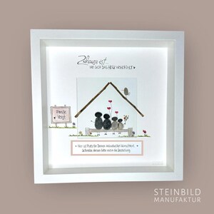 Könnte beinhalten: Ein weiß gerahmtes Bild mit einem handgemalten Kieselkunst-Design eines Hauses mit einer vierköpfigen Familie, die auf einer Bank sitzt. Der Text "Zuhause ist... WO SICH DAS HERZ WOHLFÜHLT" ist über dem Haus geschrieben. Der Text "Familie Voigt" ist auf einem Schild unter dem Haus geschrieben. Der Text "Hier ist Platz für Deinen individuellen Wunschtext. Schreibe diesen bitte mit in die Bestellung." ist unter der Bank geschrieben.