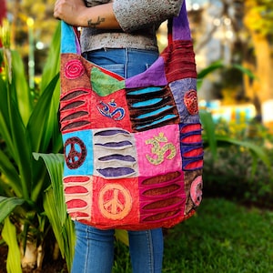 May include: A colourful patchwork shoulder bag with peace signs and Om symbols. The bag is made of different fabrics and has a distressed look.