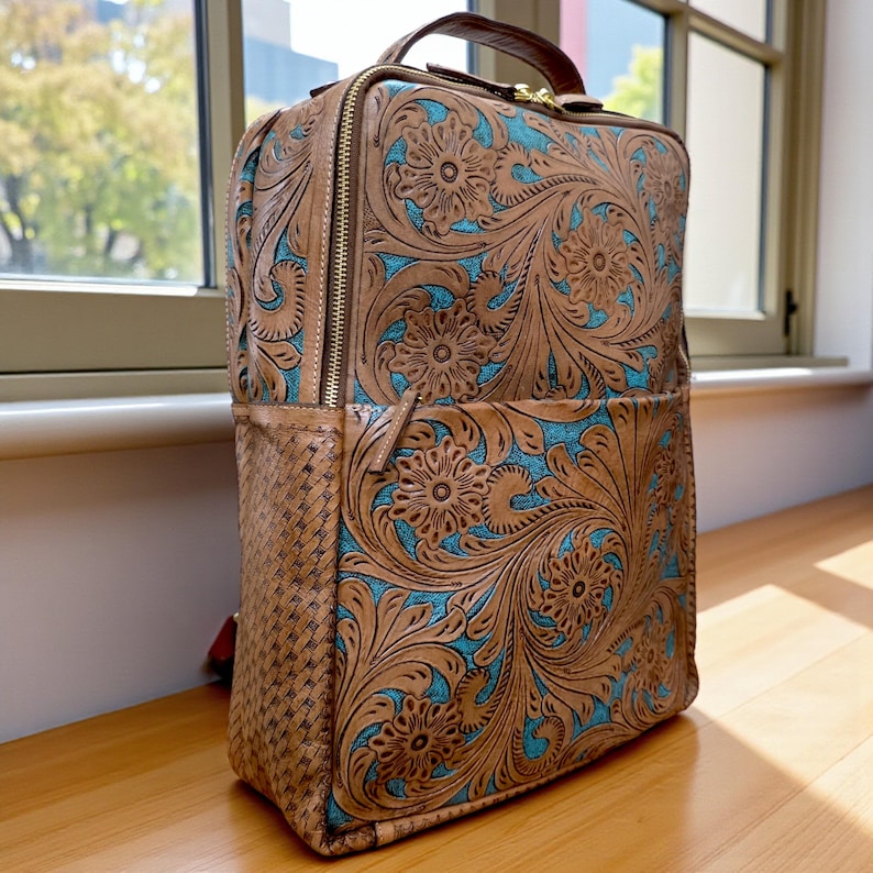 May include: A rectangular backpack featuring tan leather with intricate floral tooling and a vibrant turquoise blue textured background. The side panel displays a woven leather pattern, and the bag includes a top handle and gold-tone zippers.