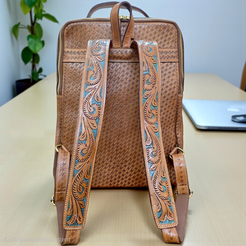 May include: A tan leather backpack featuring a woven texture pattern across the main body. The shoulder straps are decorated with intricate floral tooling and turquoise accents. The bag includes gold-tone zippers and a top carry handle.