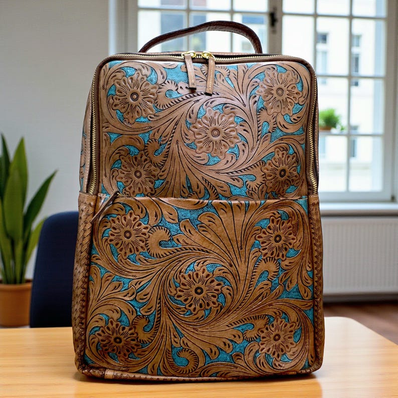 May include: A rectangular backpack featuring a tan leather exterior with an intricate embossed floral pattern. The recessed areas of the design reveal a bright turquoise blue background. The bag includes gold-tone metal zippers and a top handle.