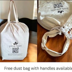 May include: An off-white cotton dust bag with two top handles and a drawstring closure. The front features the black text Bombay Blossom, a logo, a QR code, and the website address www.bombayblossom.com printed in a clear, sans-serif font.