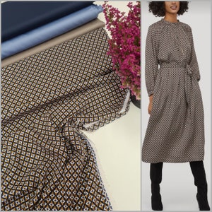May include: A brown and black geometric patterned fabric with a white trim. The fabric is folded and draped on a white surface. A woman is wearing a dress made from the same fabric.