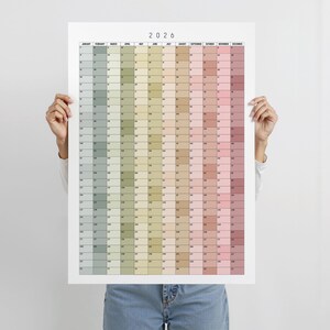 May include: A 2026 year planner poster. The calendar is divided into months, each with a different colour. The colours range from green to pink. The year 2026 is printed at the top of the poster.