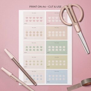 May include: A printed A4 sheet with goal-tracking charts, each with a different shape: hearts, flowers, butterflies, stars, and diamonds. The text "PRINT ON A4 - CUT & USE" is at the top. A pair of scissors, two pens, and a roll of tape are also visible.