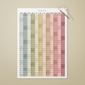 May include: A large 2026 year calendar printed on white paper. The calendar features a grid layout with each month represented by a column of squares. The squares are colored in a gradient of pastel hues. Two pens rest on the top right corner.