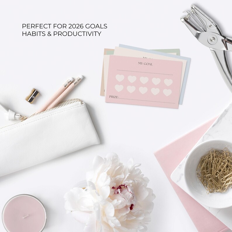 May include: A flat lay of stationery and office supplies. A white pencil case, pencils, a pencil sharpener, and goal-setting cards with heart-shaped icons are arranged on a white surface. The text "PERFECT FOR 2026 GOALS HABITS & PRODUCTIVITY" is at the top.