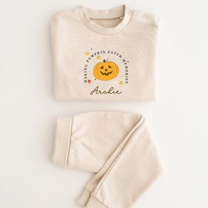 Peut inclure: Une tenue de bébé en deux pièces de couleur crème avec des manches longues et un pantalon. Le haut est orné d'un graphique de citrouille avec le texte "Making Pumpkin Patch Memories" et le nom "Archie" imprimé en dessous.