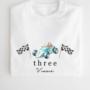 May include: White sweatshirt featuring a blue racing car and chequered flags. The text "three Vinnie" is printed below the car.