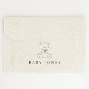 May include: A white envelope with a black line drawing of a teddy bear and the text "BABY JONES" printed on the front.