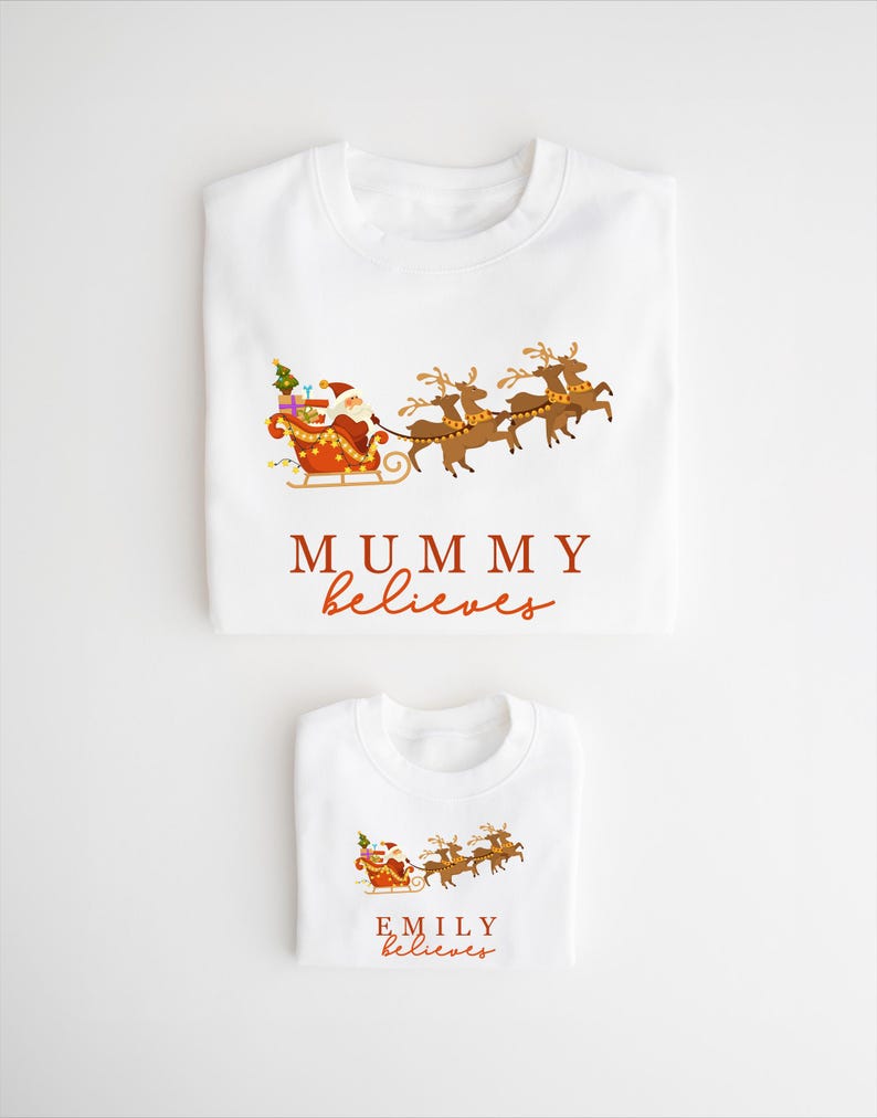 May include: Two white t-shirts with a Christmas theme. The larger shirt says "MUMMY believes" and the smaller shirt says "EMILY believes". Both shirts feature a cartoon image of Santa Claus in his sleigh pulled by reindeer.